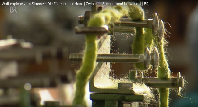 Maschine verarbeitet grüne Wollfäden zu Teppich.